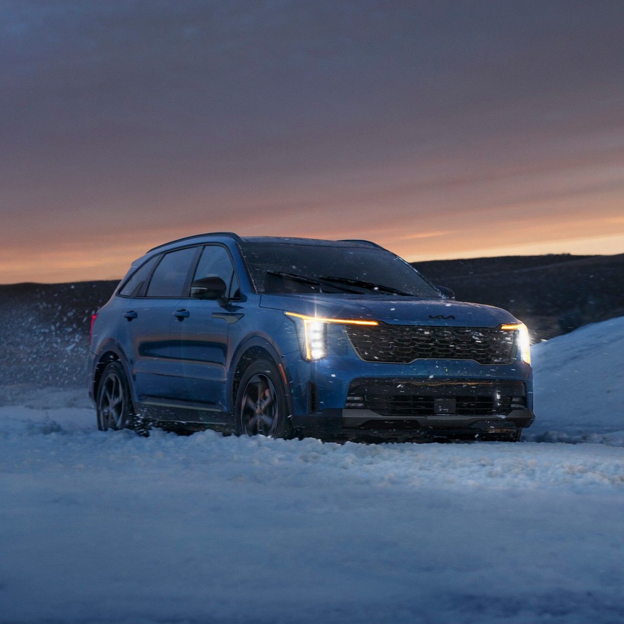 Dramatic photograph of the 2027 Kia Sorento Hybrid SUV driving through deep ice and snow in dim, dusk light, a chilly scene meant to convey a sense of exploration and power.