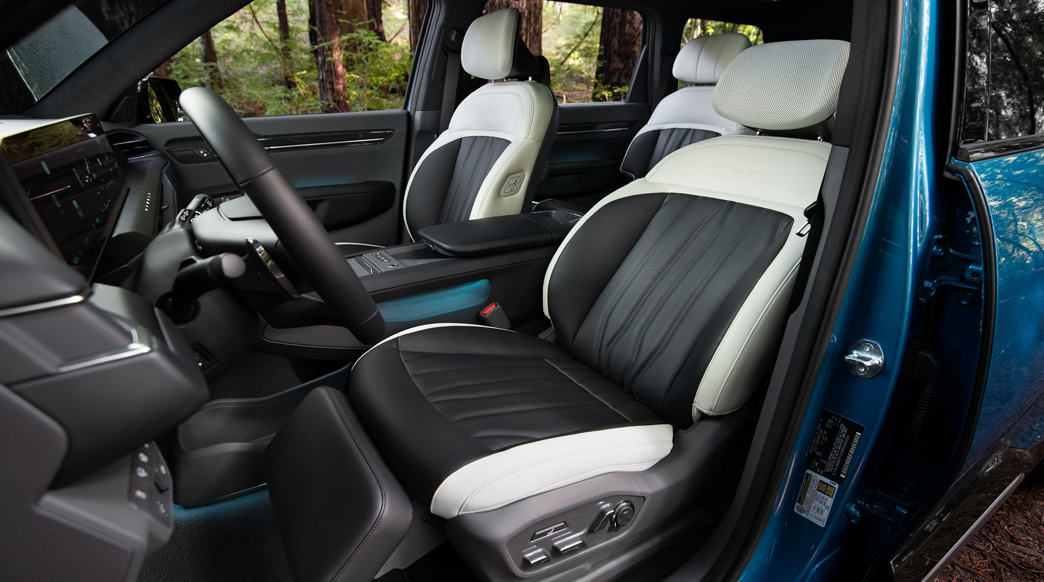 2024 Kia EV9 interior, three-quarter driver and passenger seat view from the outside with the car door open, featuring an adjustable leg rest and large lounge seats