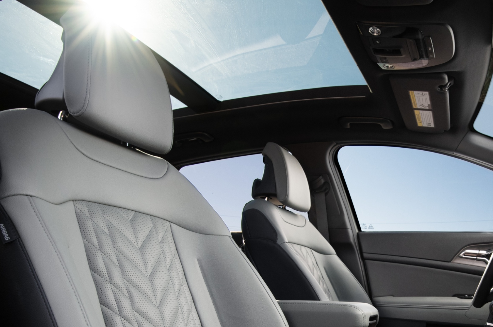 2025 Kia Sportage interior, three-quarter side view of the front seats, featuring the panoramic sunroof above them