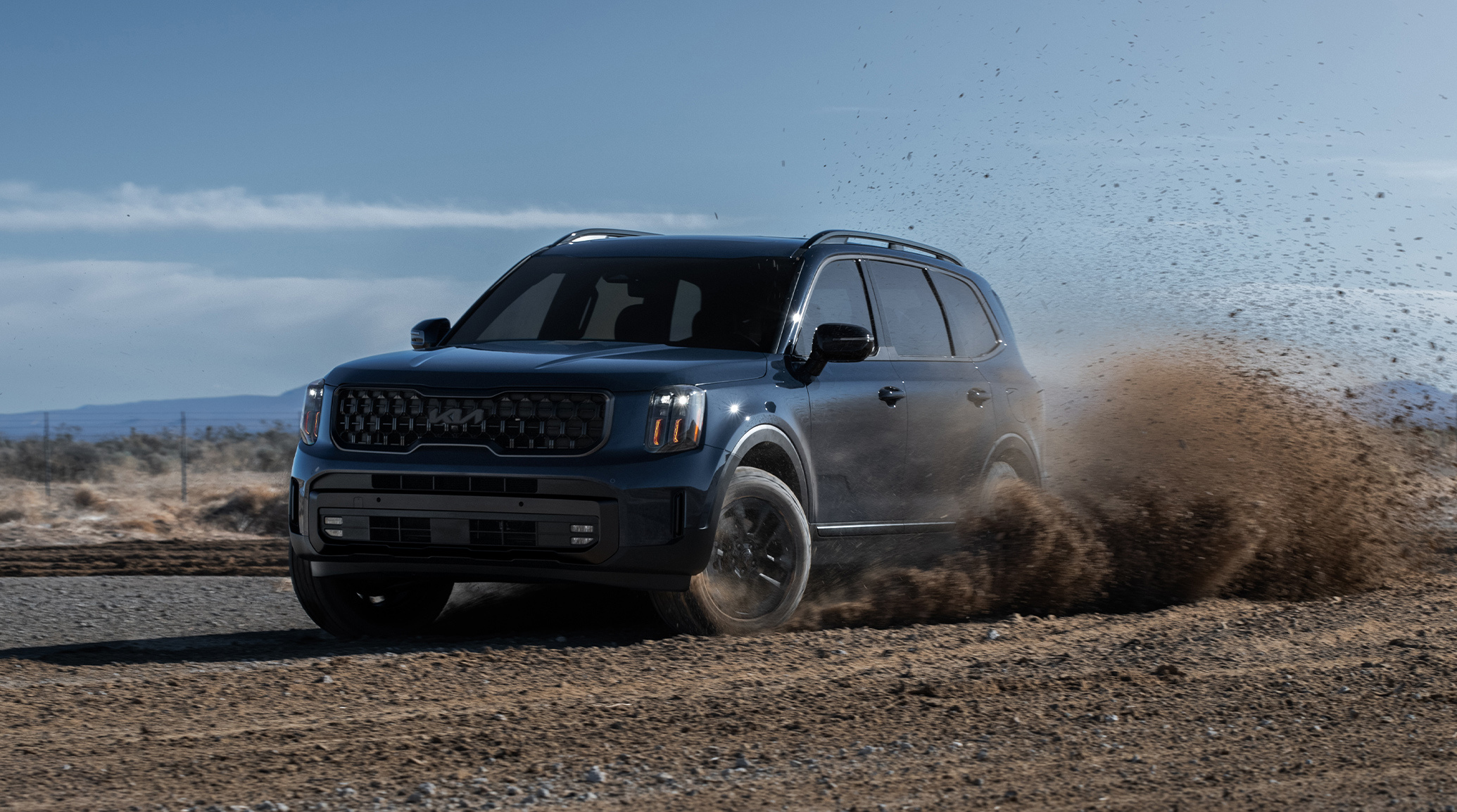 2025 Kia Telluride in a three-quarter front view, making a strong turn that causes dirt to fly in the air