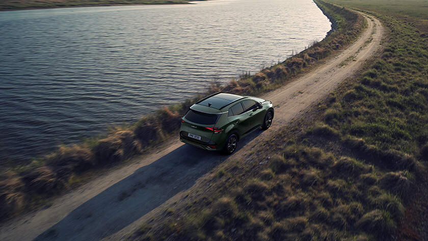 Vista amplia del KIA Sportage circulando por un camino de tierra en plena naturaleza con vistas a ríos y montañas