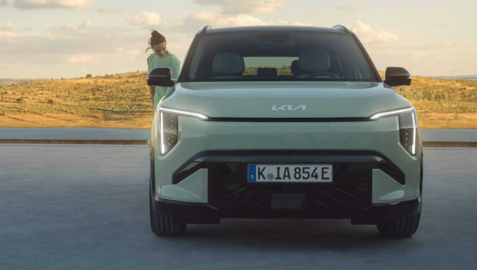 Front view of a Kia EV3 with a person standing beside it, in a scenic outdoor location.