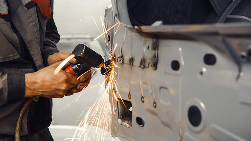 Mechanic is repairing a car body using pneumatic grinding machine 