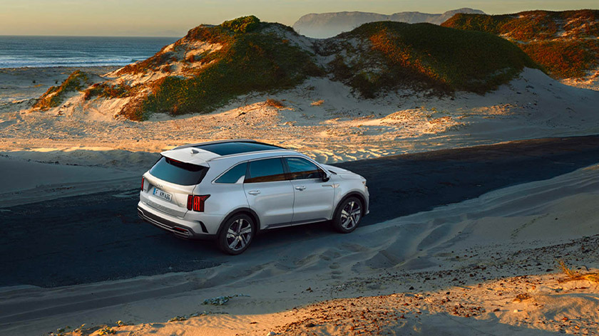 A Sorento Hybrid is driving down a winding dirt road next to a sandy beach