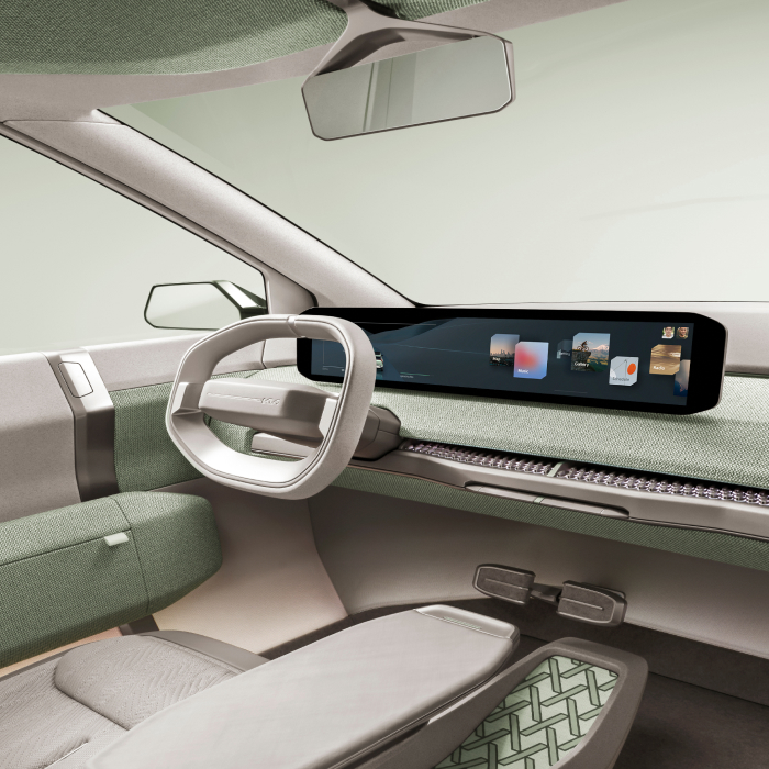 Kia EV3 concept vehicle interior, driver's seat view, featuring a panoramic digital screen and light green interior accents.