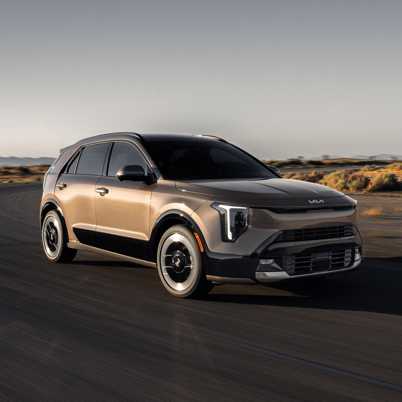 Front passenger side angle photograph of the 2027 Kia Niro Hybrid Electric SUV driving around a curved desert road in the sun.